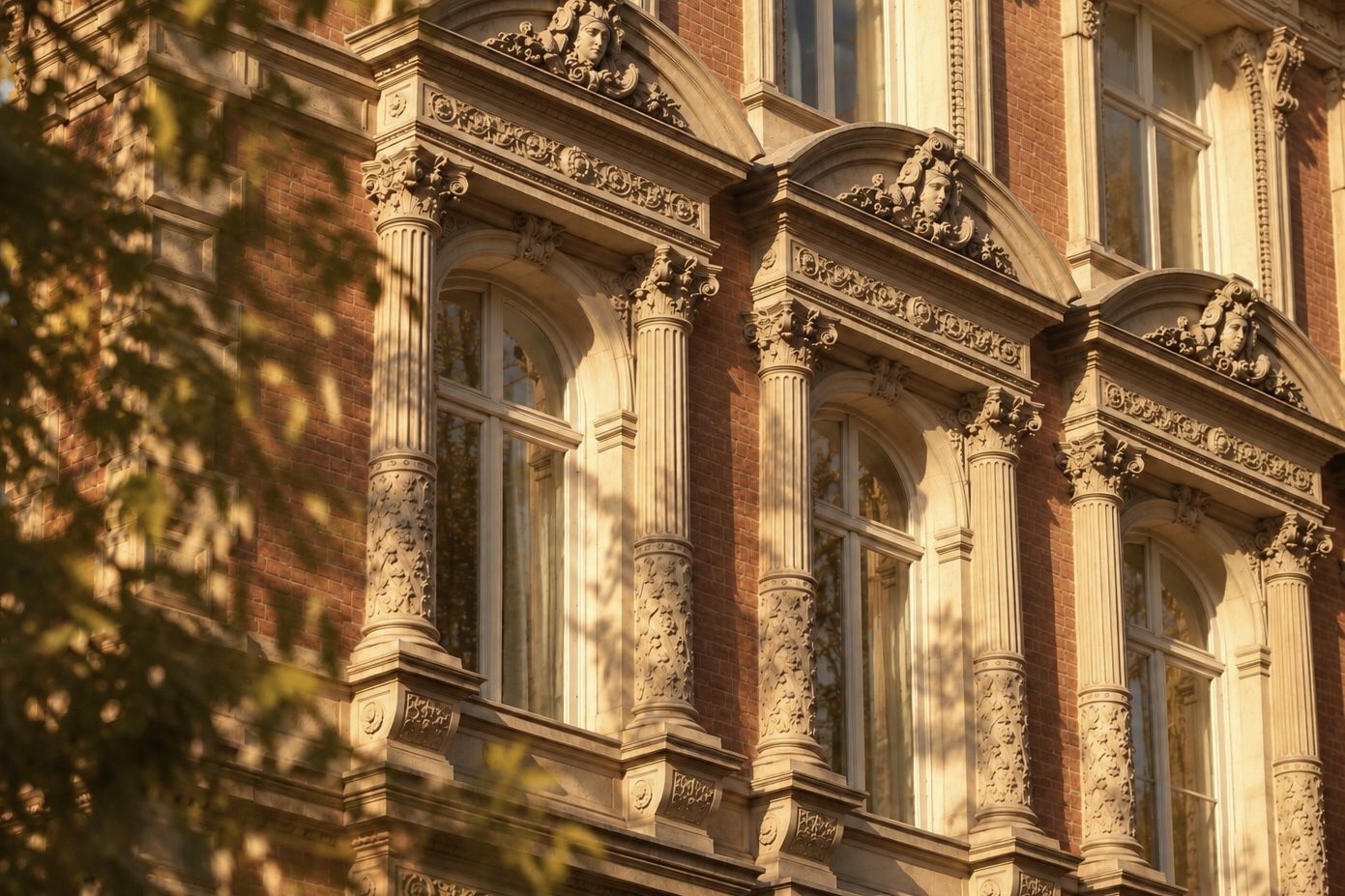 A brick and carved stone facade with tall arched windows in late golden light